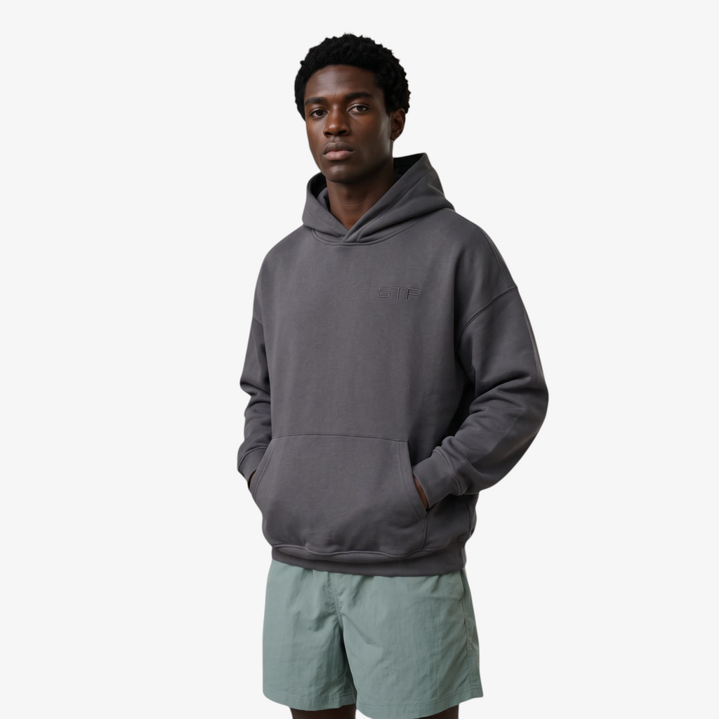 Model wearing a Seejthreadsflames (STF) charcoal grey heavyweight oversized French terry hoodie with chest embroidery.