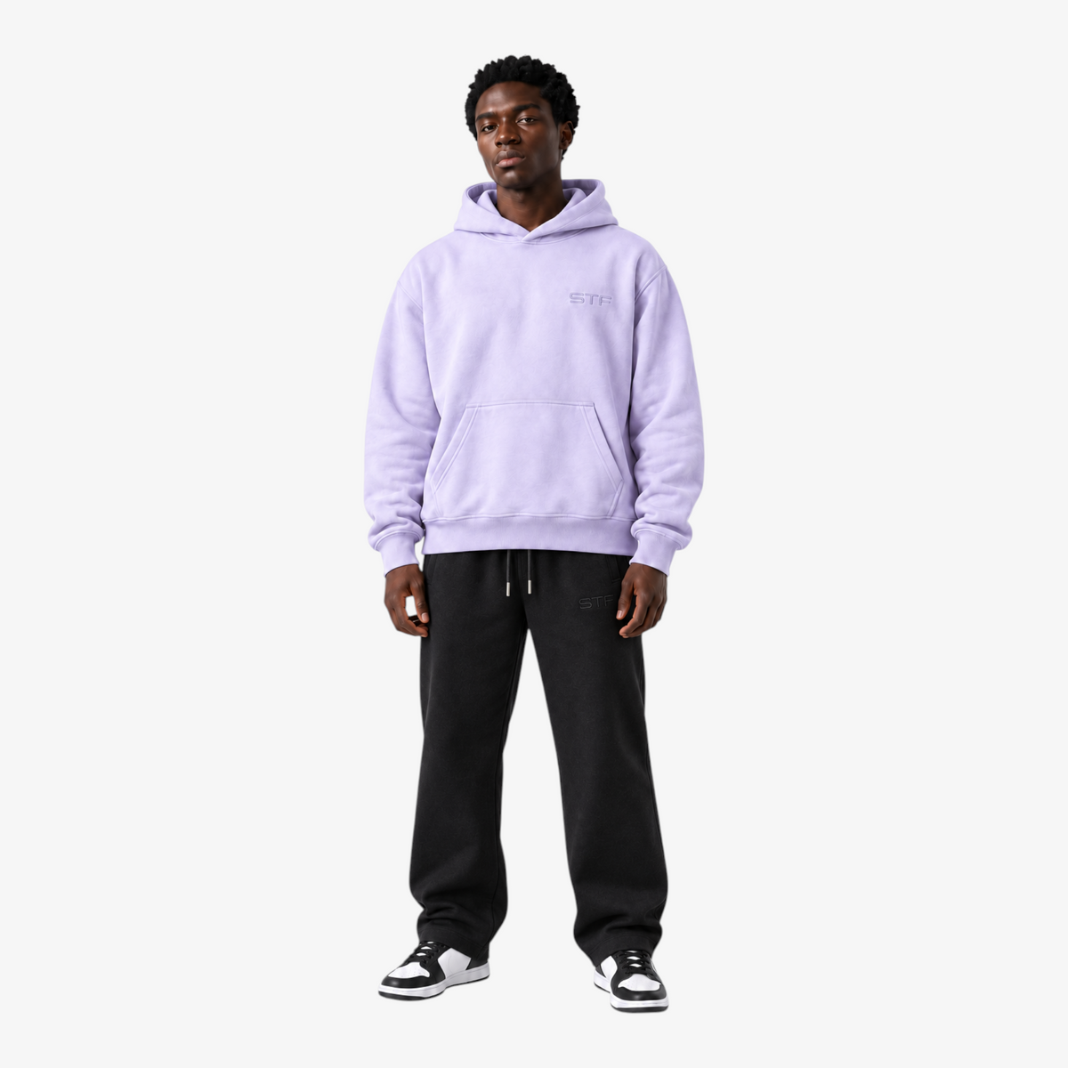 Model wearing a Seejthreadsflames (STF) lavender pullover hoodie with chest embroidery and black sweatpants